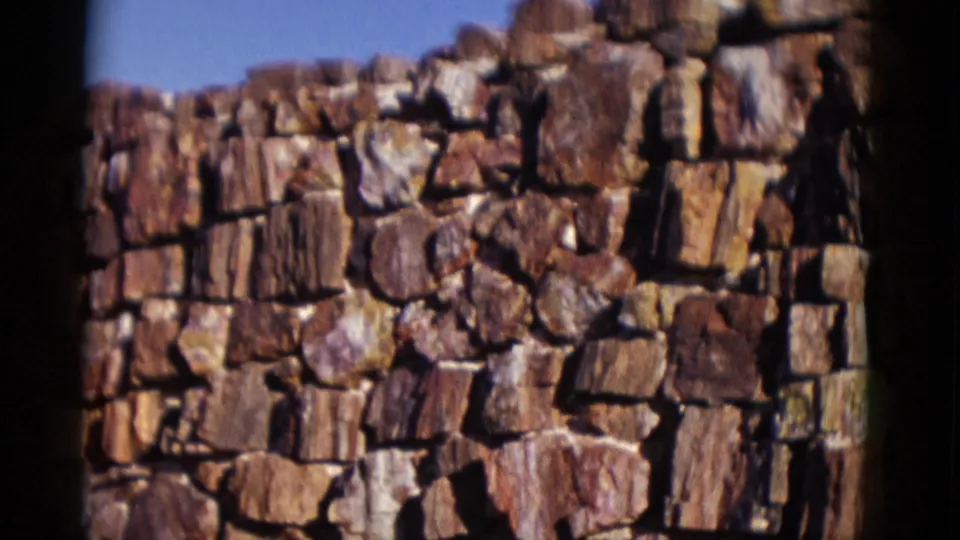 1952 Arizona frame showing a flat run of rough stone wall, with varied red, brown, and pale stones in loose-fitting masonry.