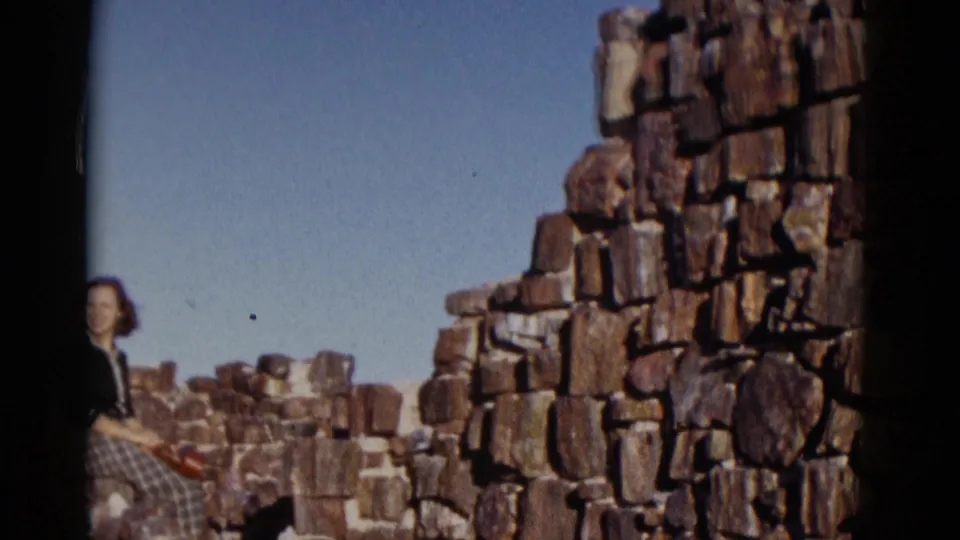 Arizona 1952 frame with a woman partly at the left edge near rugged stonework, wearing a dark top and plaid skirt.