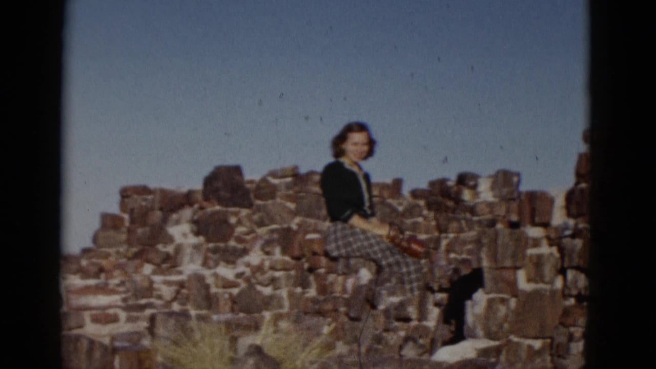 Woman sitting on a low stone wall with open sky behind her.