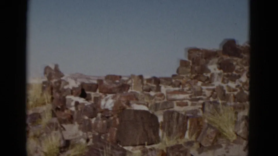 The final frame holds on weathered stone ruins, sparse desert grass, blue sky, and distant terrain in Arizona.