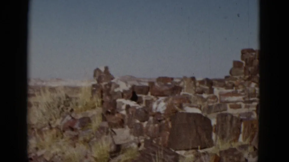 1952 Arizona 8mm frame showing weathered rocks, sparse grass, and low stone formations in an open desert landscape.