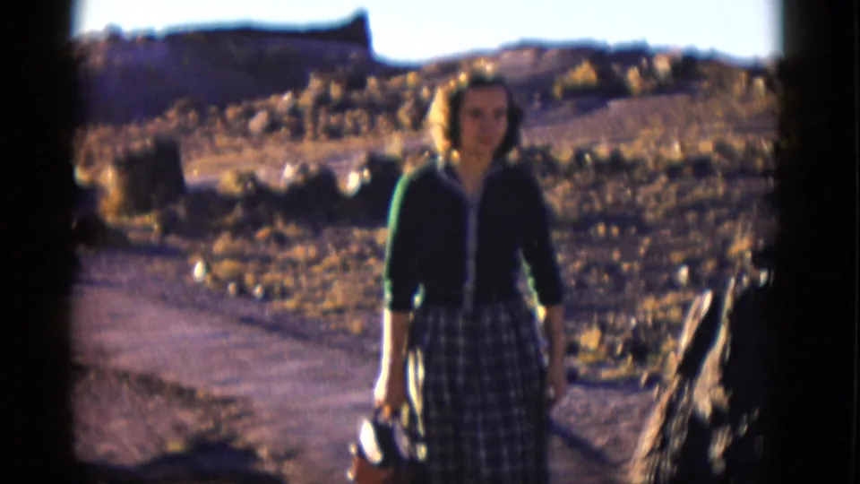 1952 Arizona 8mm frame showing a woman in a green cardigan and plaid skirt facing the camera near the Rainbow Forest area.