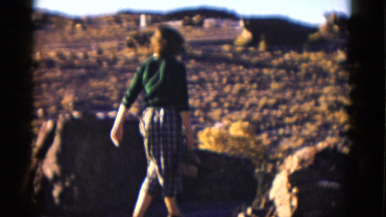 Woman walks past large rocks in a dry open desert setting.