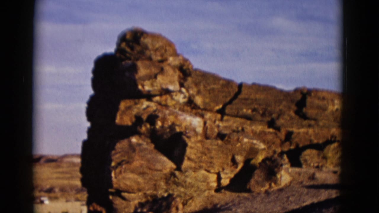 Large weathered rock formation beside a low line of stones under blue sky.