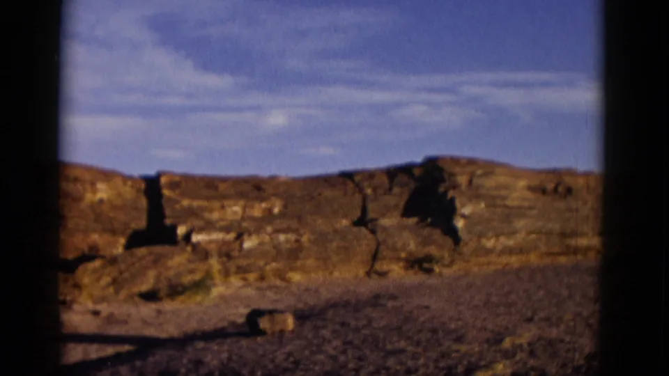 1952 Arizona home-movie frame showing the rock line from farther along the pan, with desert ground and long shadows.