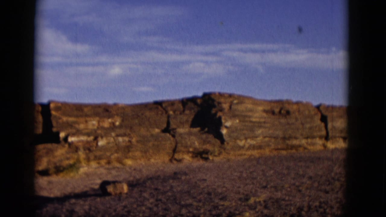 1952 Arizona 8mm frame showing sunlit layered rock ledges, gravelly foreground, thin clouds, and dark gate-edge borders.