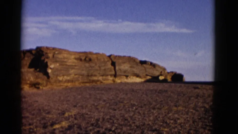 Final 1952 Arizona frame showing rock ledges, open desert floor, blue sky, wispy clouds, and visible film-frame borders.
