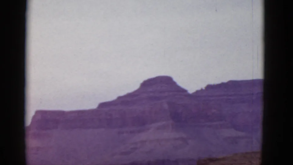 1952 Arizona home-movie frame showing distant layered desert cliffs under a pale sky, viewed from a vehicle-like position.