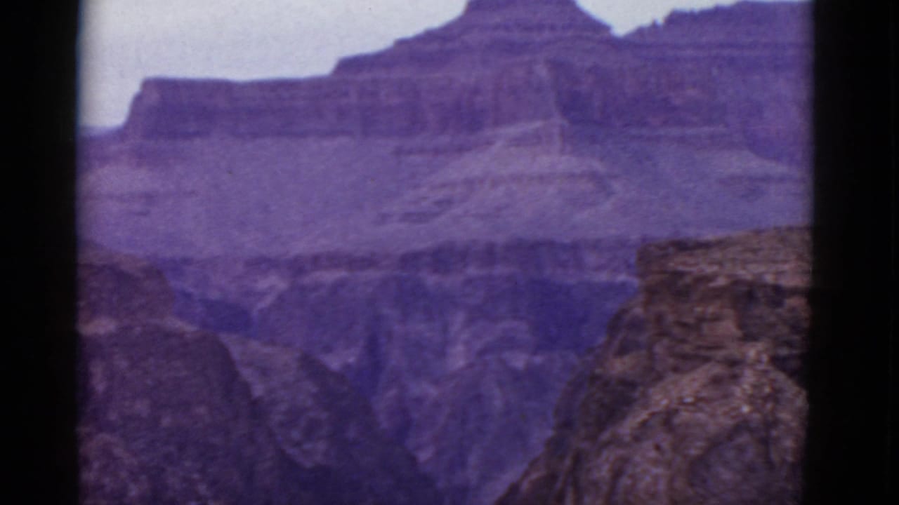 1952 8mm view of the Grand Canyon in Arizona, showing layered cliffs, distant mesas, and a pale sky with aged purple color.