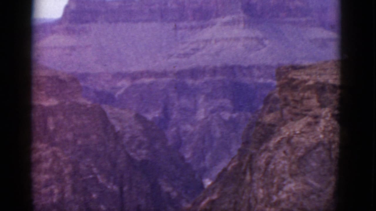 1952 Grand Canyon panorama in Arizona with purple-shifted color, distant rock layers, and a foreground cliff at right.