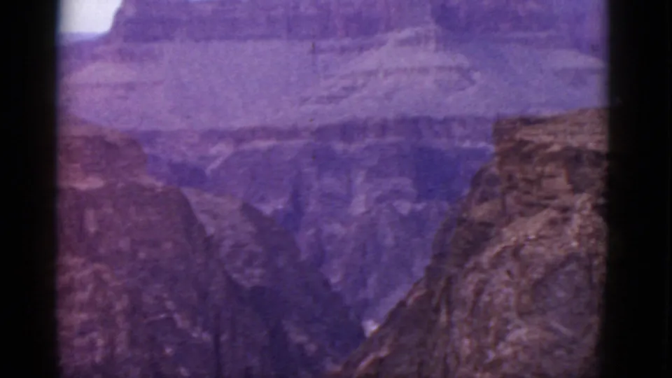 1952 Grand Canyon panorama in Arizona with purple-shifted color, distant rock layers, and a foreground cliff at right.