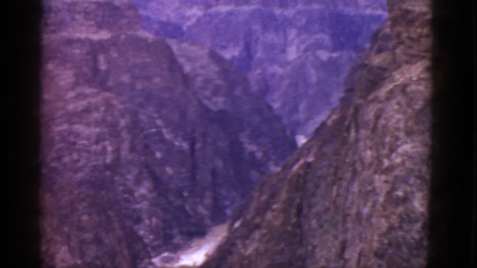 1952 Arizona Grand Canyon frame with rocky foreground wall, distant cliffs, shadowed ravine, and aged purple 8mm color.
