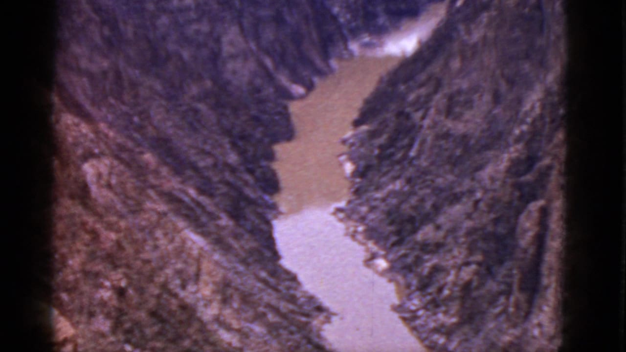Vintage 8mm view of a muddy river bend framed by rugged Arizona valley walls, with visible film edge darkening.