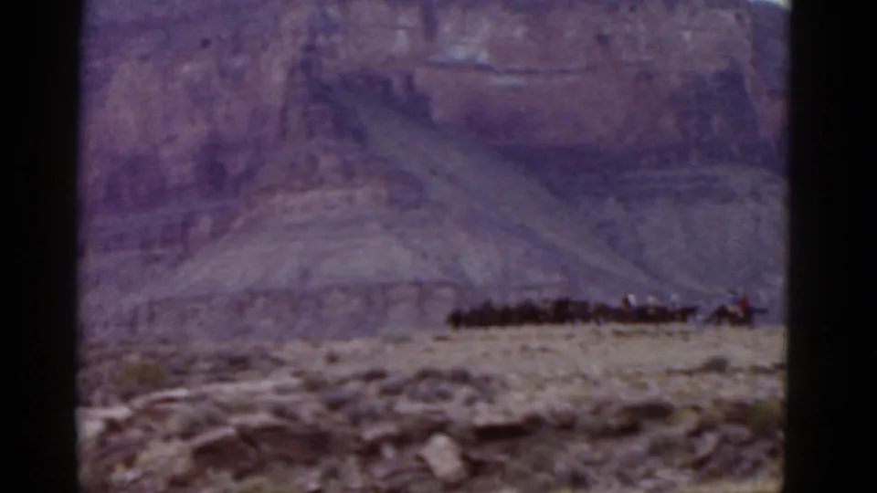 Soft 1952 Arizona 8mm frame showing a distant horse caravan crossing rocky desert with cliffs filling the background.