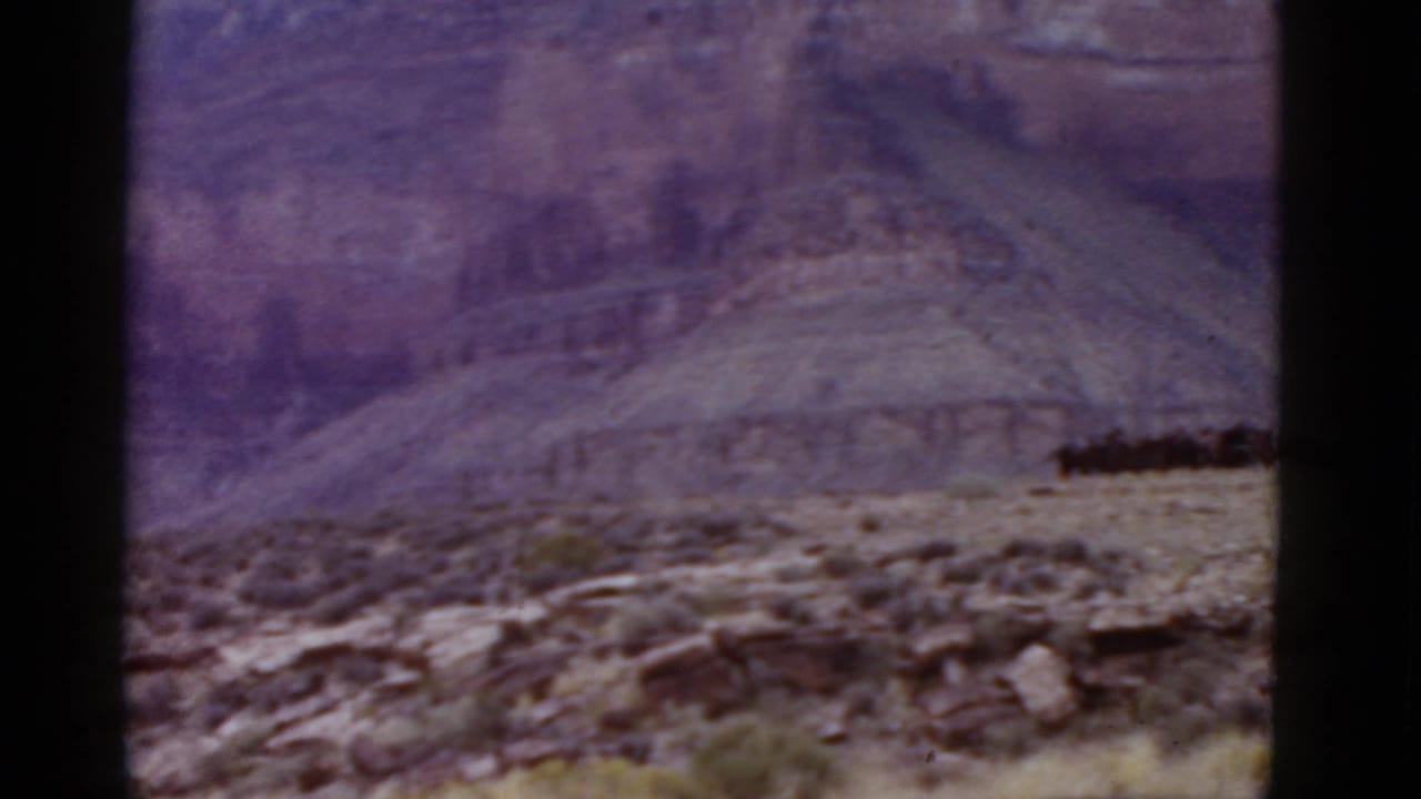 Rocky desert foreground with sparse scrub and distant canyon walls under a hazy sky.