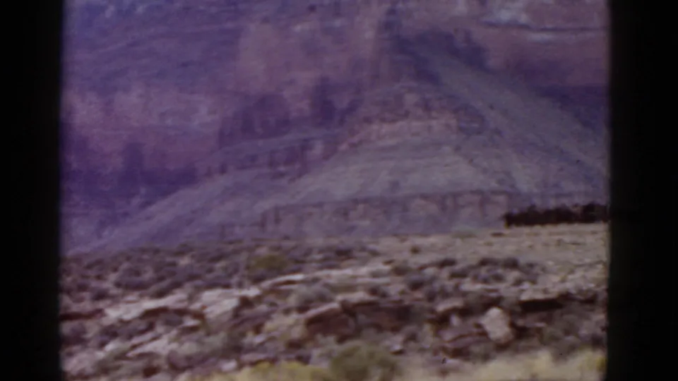 1952 Arizona home-movie frame showing rocky desert terrain and layered canyon walls with a purple-tinted 8mm film look.