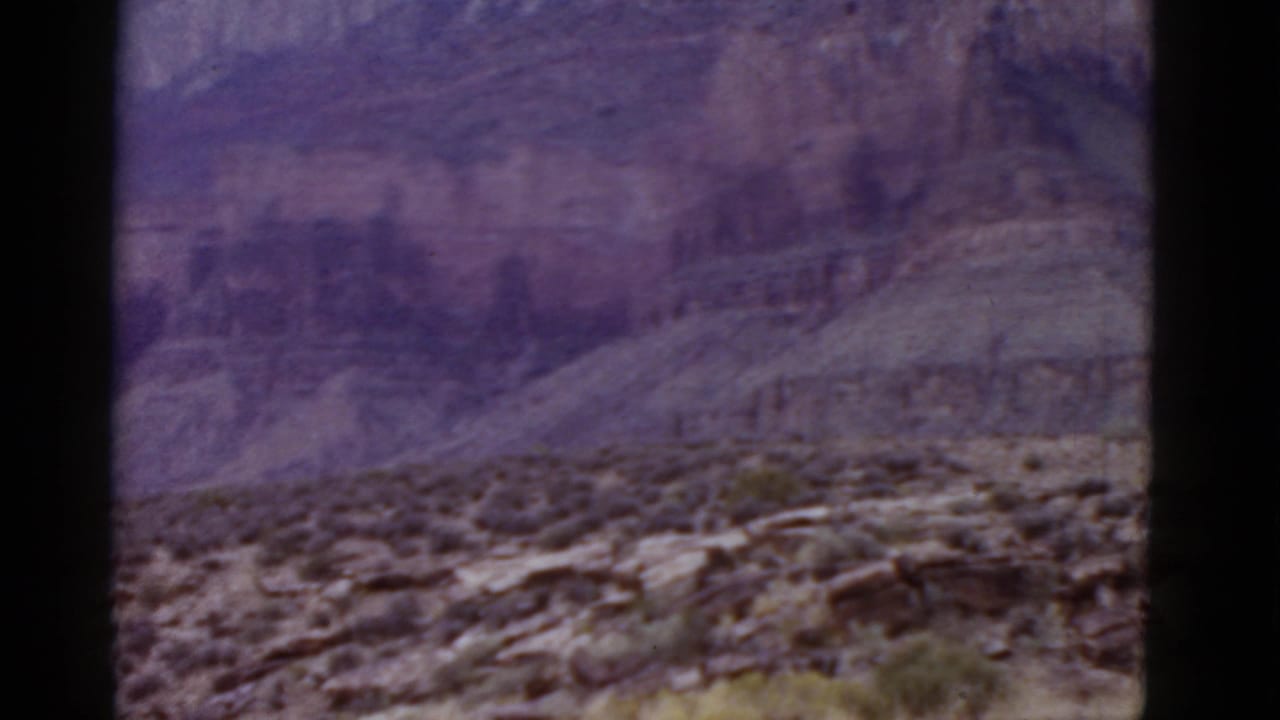 Layered canyon slopes behind rocky desert terrain with sparse vegetation.