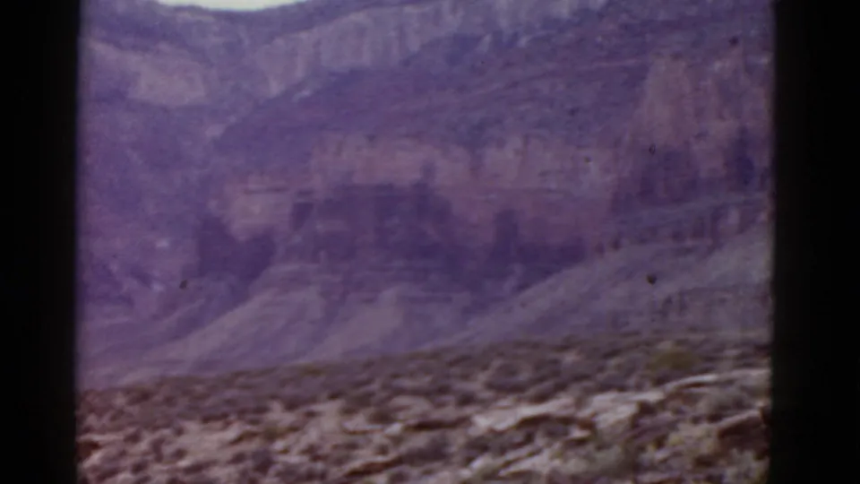 Soft, purple-shifted 8mm view of an Arizona canyon wall above a stony desert foreground, with no people or structures visible.