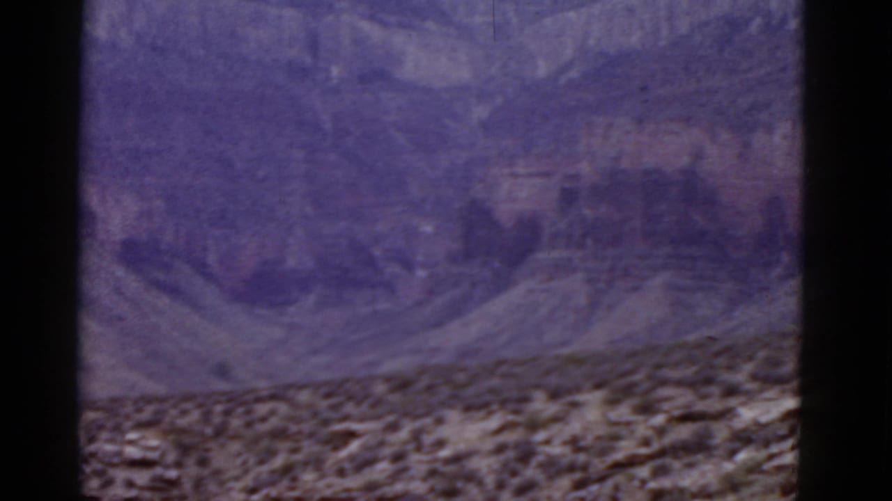 Layered desert cliff and rocky scrub foreground with dark film borders.