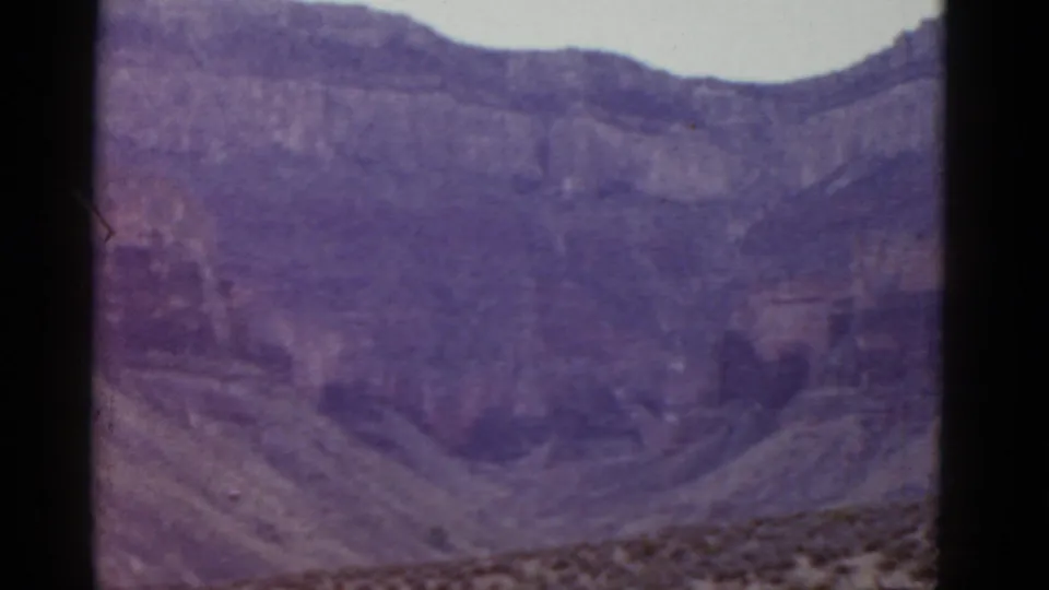 1952 Arizona 8mm view of a broad cliff wall and arid foreground, tinted by aged purple film color.