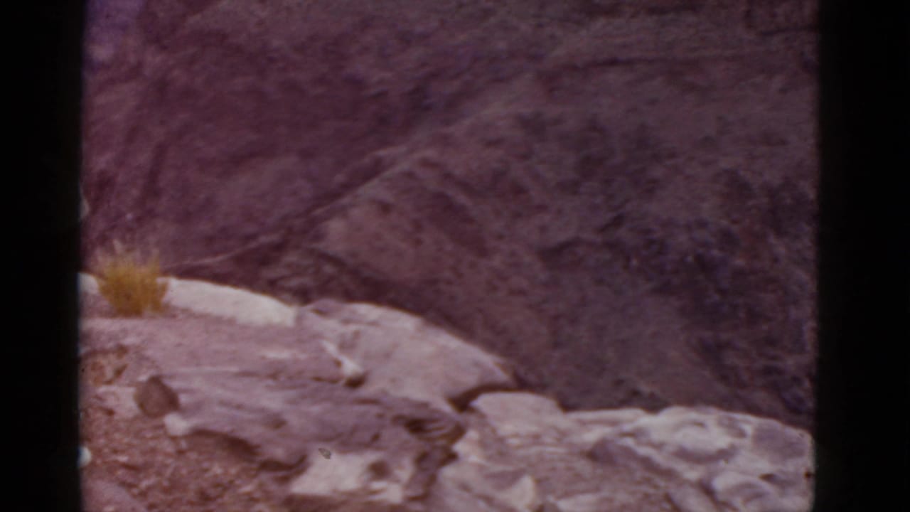 Rocky canyon overlook with a partial figure at the left edge and dark film borders.