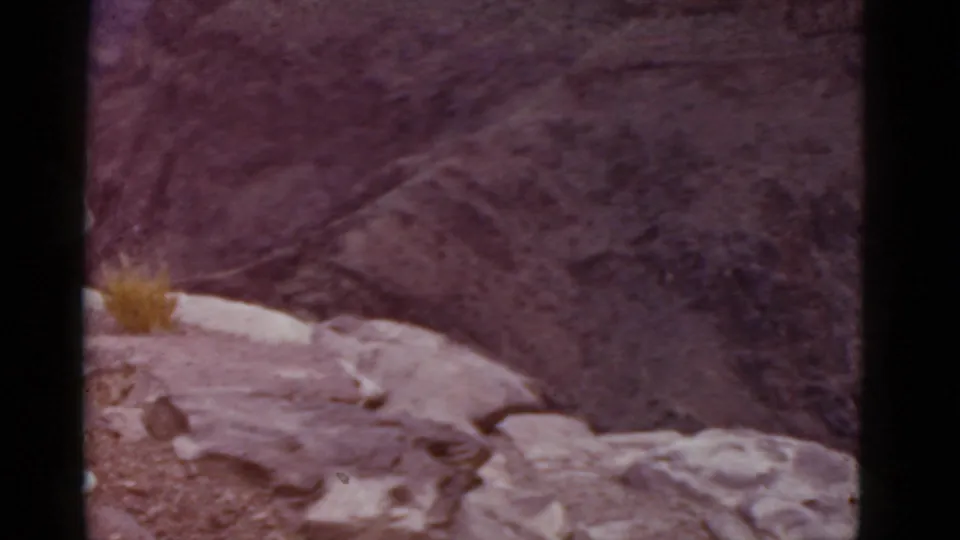 1952 Arizona home-movie frame showing a rocky overlook above a canyon, with only part of a visitor visible at the left edge.