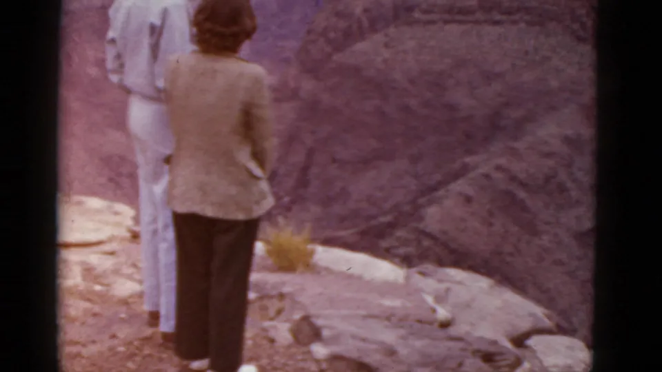 1952 Arizona home-movie frame showing two adults from behind at a rocky canyon overlook, one in a light suit and one in a jacket.