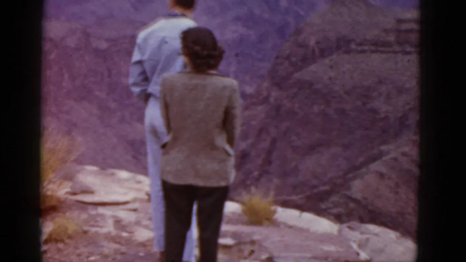 1952 Arizona vacation frame with a couple standing close together at a canyon overlook, surrounded by rock and sparse grass.