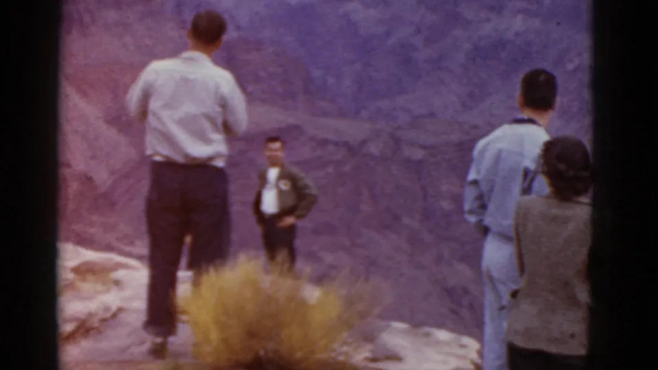 1952 Arizona home-movie frame with adult visitors arranged along a rocky canyon overlook.