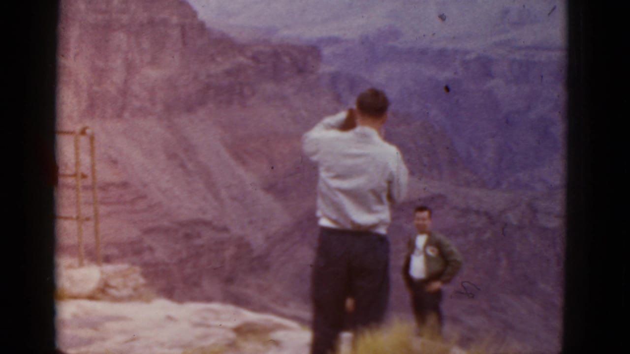 1952 Arizona home-movie frame showing one man photographing a canyon view while another man stands near the overlook.