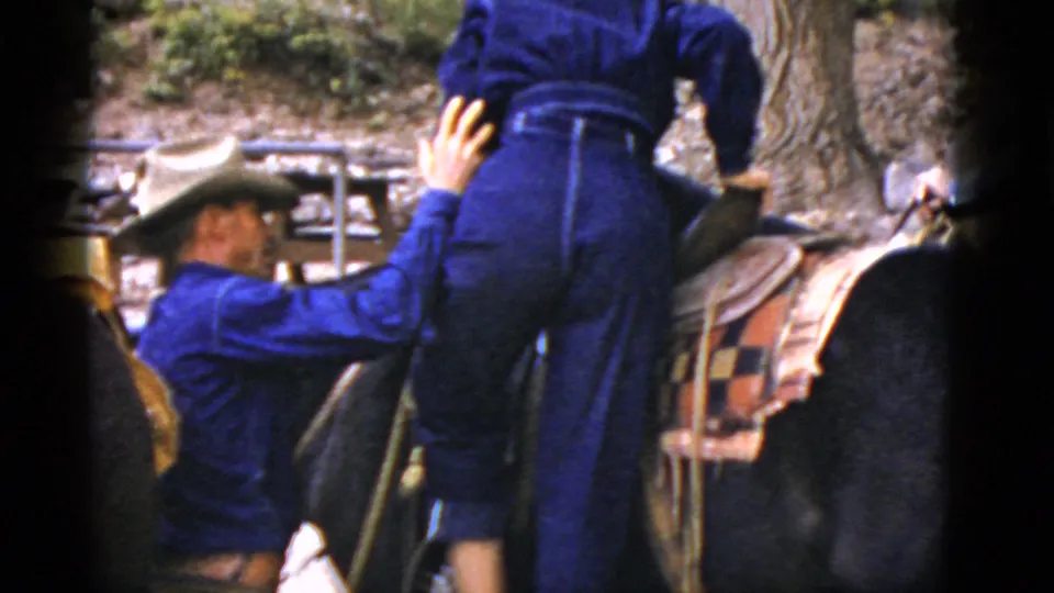 The woman continues mounting the horse as the man supports her, with saddle blanket and trees visible in the Arizona setting.