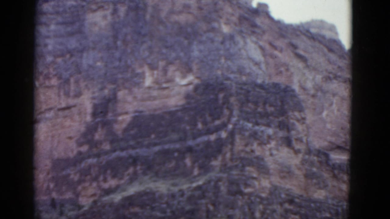 Close view of a rugged cliff wall with pale sky above and dark film borders.