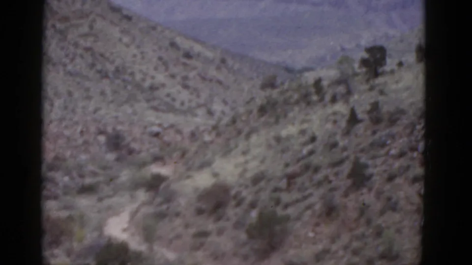 1952 Arizona 8mm frame looking over a rugged desert hillside, winding path, shrubs, and hazy distant terrain.