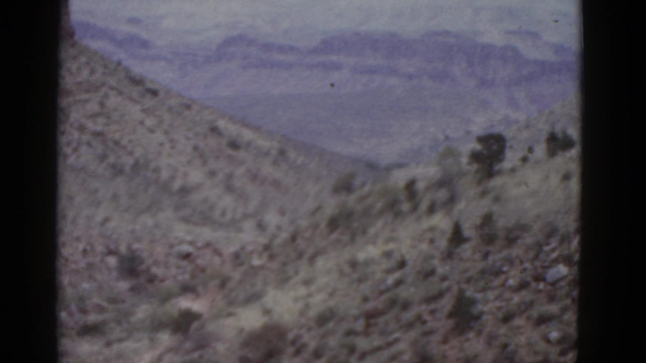 Rocky desert hillside with sparse scrub and distant hazy mountain layers.