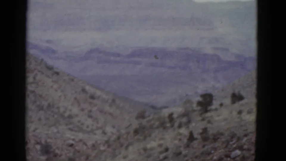 1952 Arizona travel footage frame with a sloping desert foreground and broad, hazy mountain range beyond.