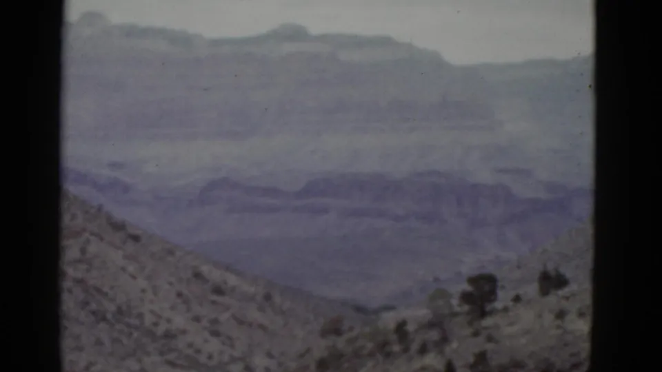 1952 Arizona 8mm frame showing rocky desert foreground, sparse vegetation, and layered distant highlands.