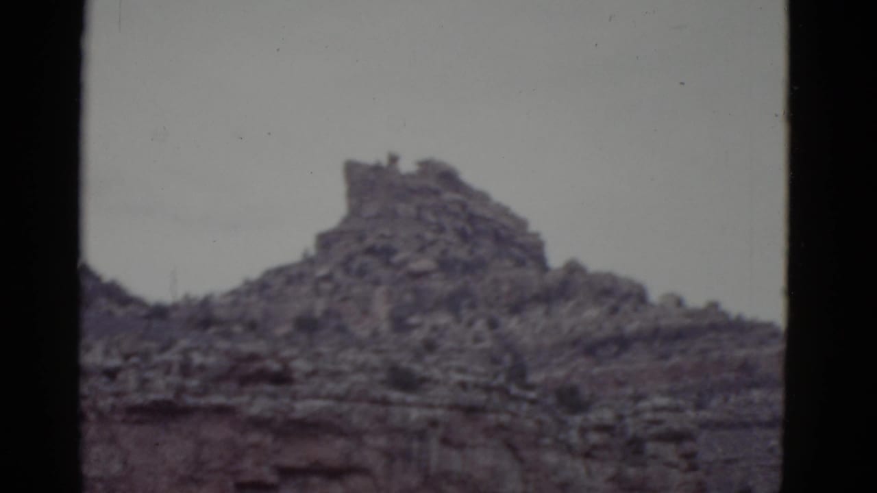 1952 Arizona 8mm frame showing a rugged mesa crest, layered rock face, sparse vegetation, and dark film borders.