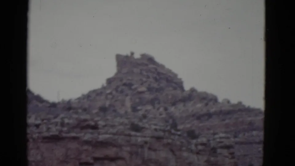 1952 Arizona 8mm frame showing a rugged mesa crest, layered rock face, sparse vegetation, and dark film borders.