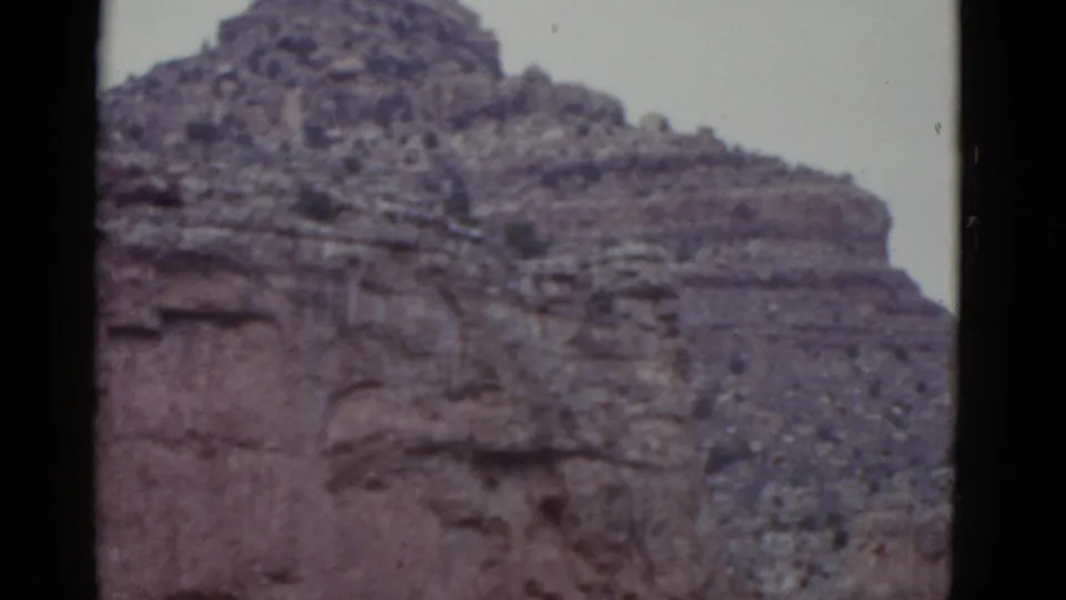 1952 Arizona 8mm frame showing a layered cliff wall below a rough mesa top, with sparse desert growth and visible film borders.