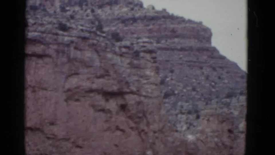 1952 Arizona 8mm frame capturing a broad desert rock formation with layered cliff bands, scattered vegetation, and soft archival color.
