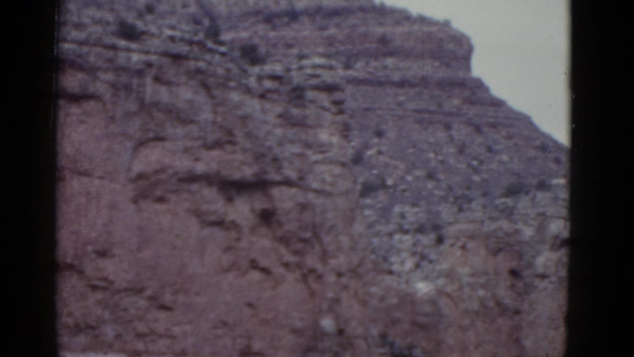 1952 Arizona 8mm frame showing reddish layered Grand Canyon rock beneath pale sky.