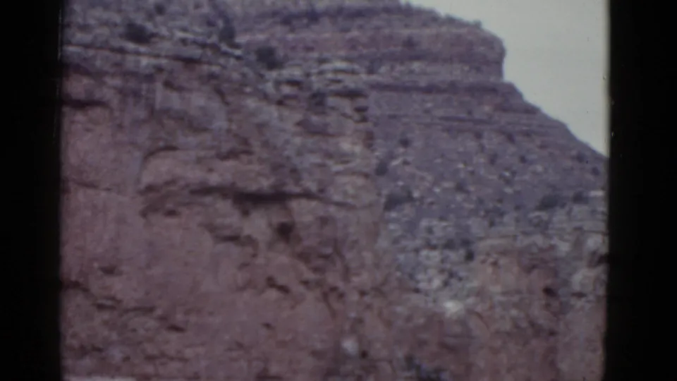 1952 Arizona 8mm frame showing reddish layered Grand Canyon rock beneath pale sky.