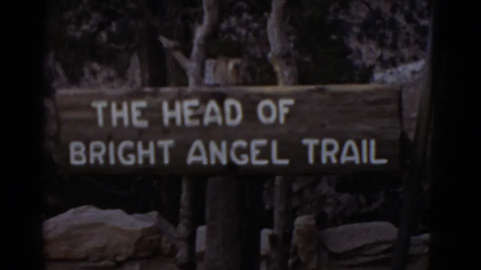 1952 Arizona 8mm frame with a wooden sign for the head of Bright Angel Trail in a shaded area.