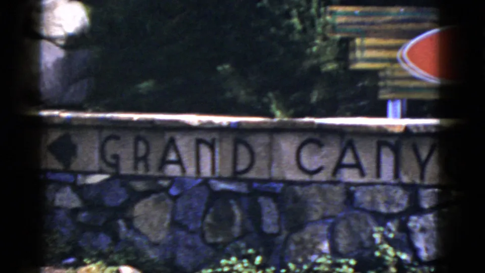 1952 Arizona frame with carved Grand Canyon lettering on a stone wall and part of a red directional arrow sign above it.