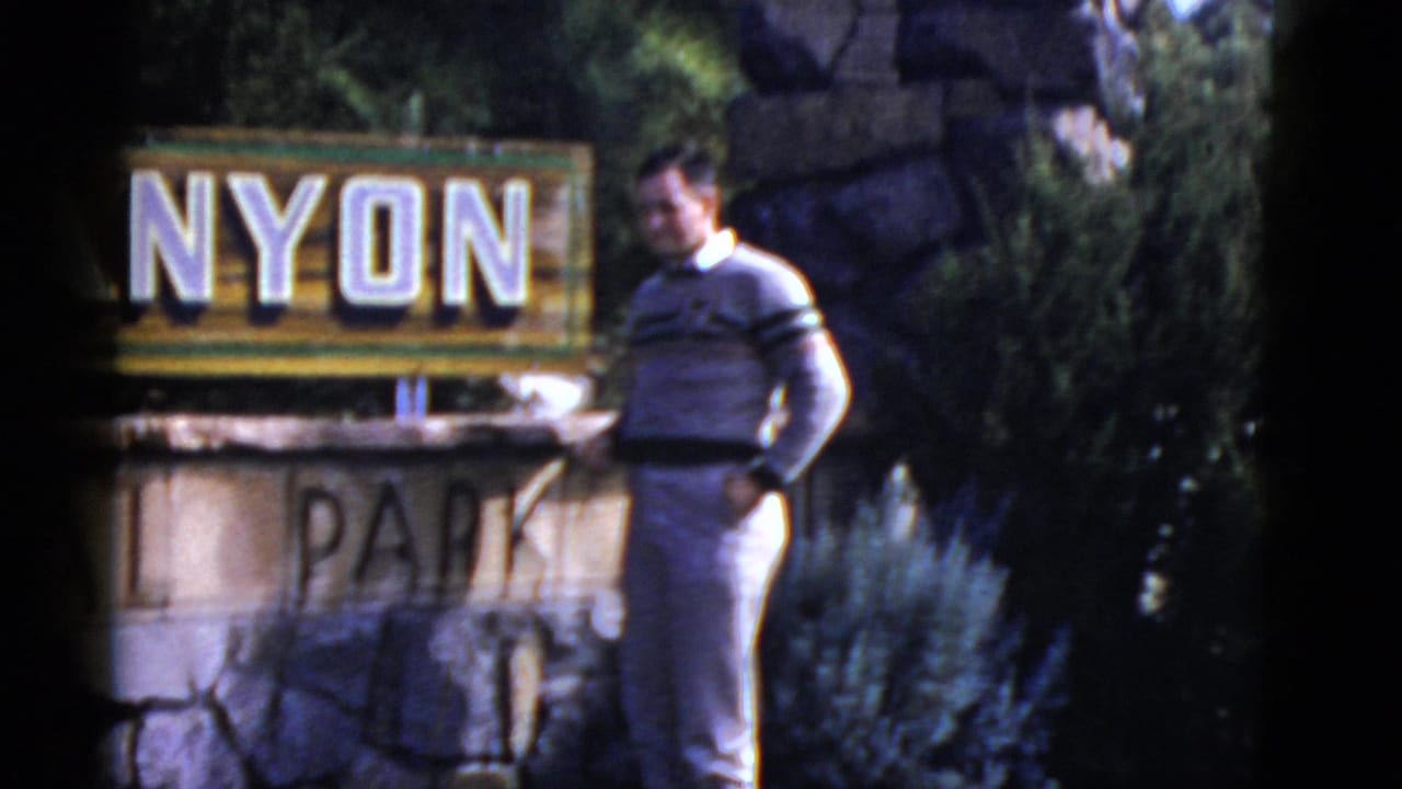 Man standing beside a partial park sign with trees behind him.