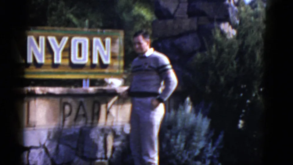 Adult man in a striped sweater stands beside a stone park sign in California, from 1952 home-movie footage.