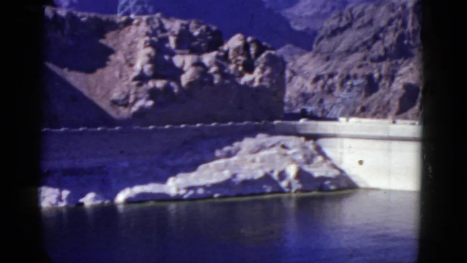 Reservoir and dam view in mountainous California terrain, seen in grainy color 8mm footage from 1952.