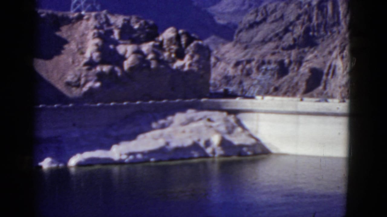 Concrete dam and reservoir below rocky mountains in a soft, blue-tinted 8mm frame.