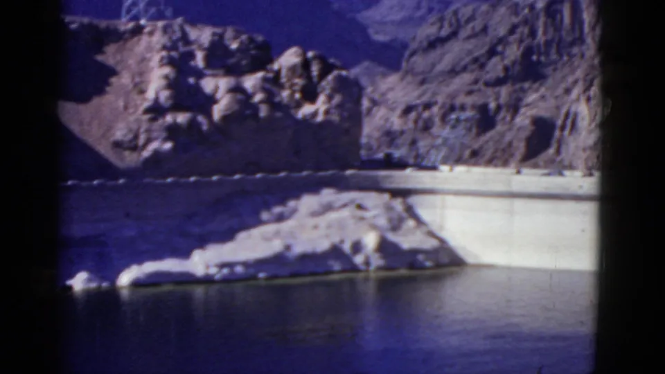 1952 California home-movie view of a concrete dam, calm reservoir water, and rugged rocky slopes seen from a distance.