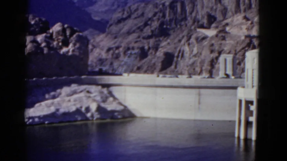 A wider 1952 California dam view shows reservoir water, the concrete wall, rugged slopes, and pale tower-like structures on the right.